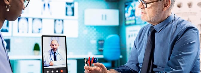 Doctor holding a virtual meeting with a distant health specialist on a tablet screen.