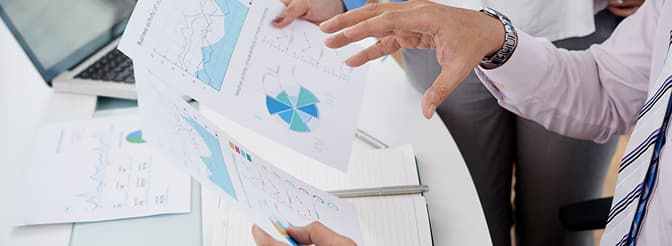 Business professionals reviewing and discussing printed financial charts and graphs at a desk.