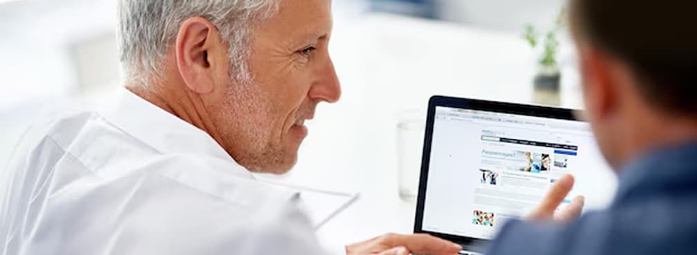 Senior doctor looking at a medical dashboard website on a laptop screen with a colleague.