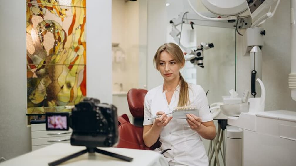 A dentist filming a medical demonstration with a camera on a tripod at her practice.
