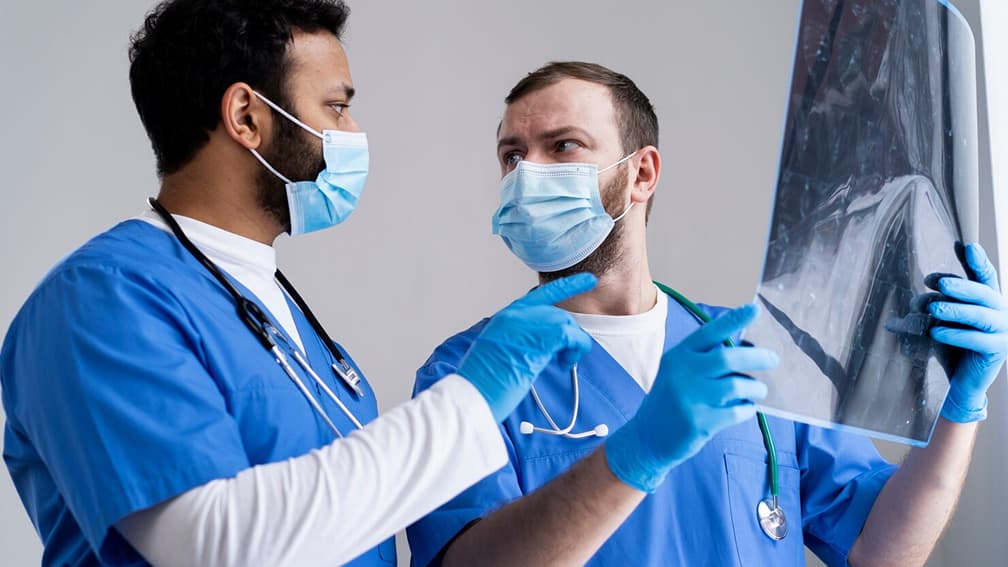 Healthcare professionals wearing medical gloves and masks while analyzing an X-ray.