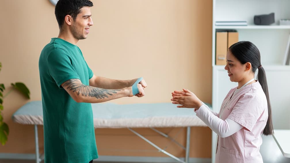 A clinic practitioner demonstrating physical therapy wrist stretches to a young man.
